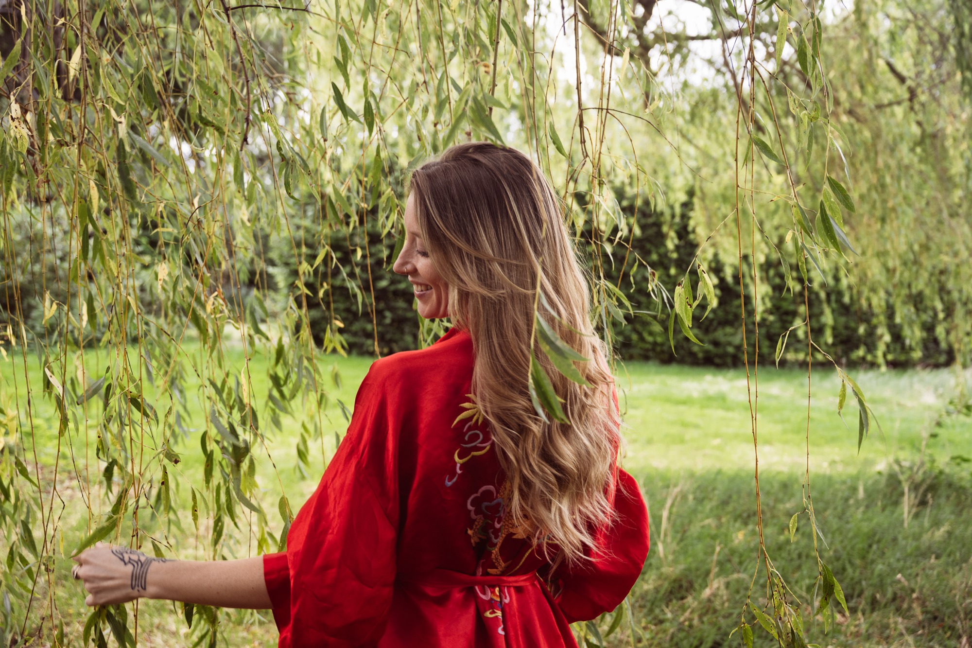 Jessica laughing beneath a willow tree in red silk